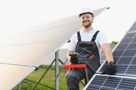 Smiling technician wearing hardhat and safety glasses, installing solar panels, contributing to...