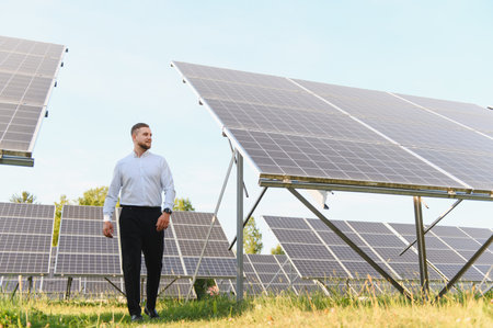 Male engineer walking through a solar panel farm, checking sustainable energy production and green...