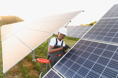 Young black technician working on solar panels, installing renewable energy system in a solar park...