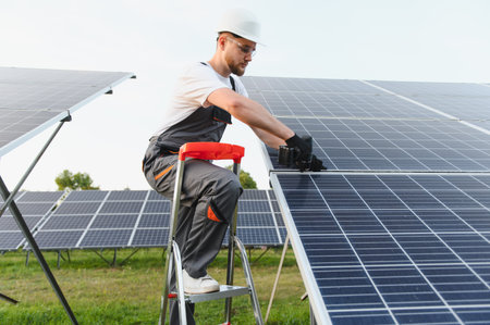 Worker on a ladder installing a solar photovoltaic panel at a large solar farm, generating...