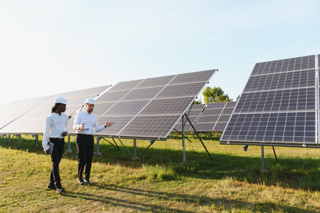 Engineers in hard hats inspecting and discussing work at a solar panel field, focusing on renewable...