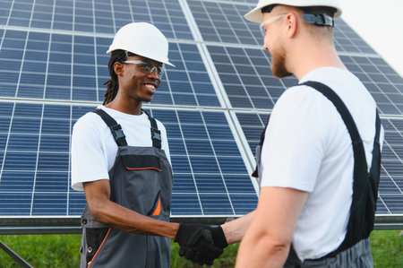 Two diverse engineers shaking hands, celebrating success and teamwork against a background of solar...