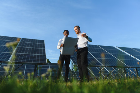 Diverse engineers reviewing plans at a solar power station, focusing on teamwork and sustainable...