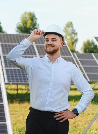 Young male engineer in hard hat smiling confidently while standing at a solar farm, symbolizing clean renewable energy progressの写真素材