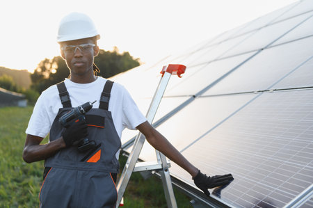African american technician holding a drill, installing solar panels, focusing on green energy and renewable power generationの写真素材