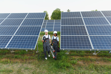 Two diverse technicians walking among rows of solar panels, carrying tools, and installing clean...