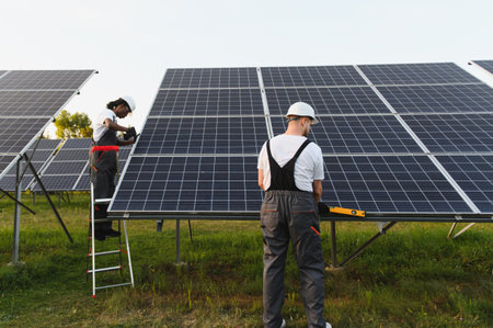 Male workers installing large solar panels in a green field, contributing to sustainable energy and...