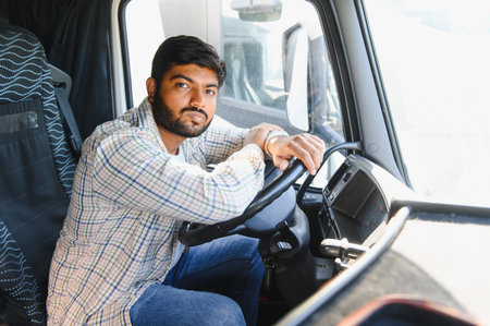 Young Indian man portrait inside truck cab, confidently holding the steering wheel, representing...