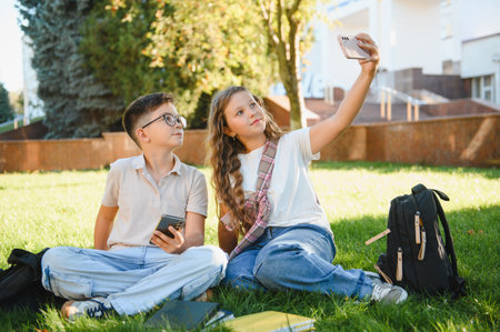 Young students creating memories by taking a selfie with a smartphone, sitting on green grass during...