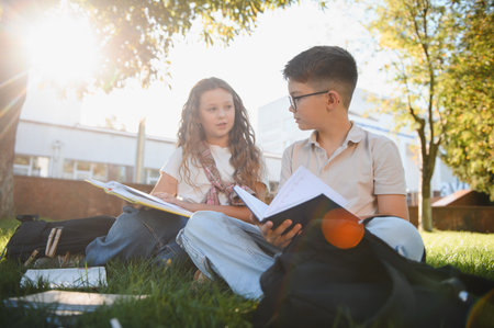 School children learning together, sitting on the green grass, discussing homework and sharing notes...