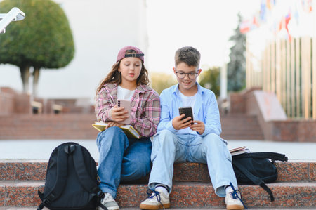 Students sitting outside, engrossed in their mobile devices, representing youth, education, and the...