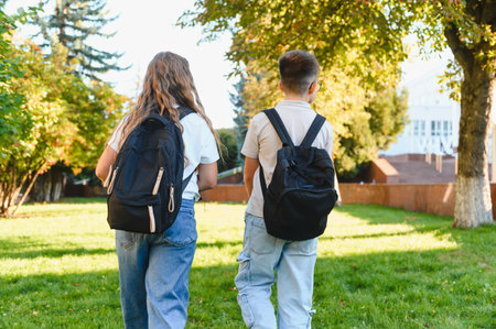Schoolchildren with backpacks walking across a green lawn towards a school building. Back to school conceptの写真素材