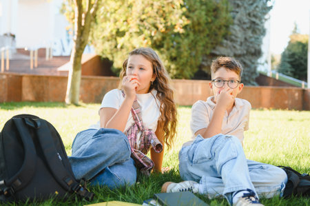 School children having a healthy snack break, eating apples and relaxing on green grass after class on a sunny school dayの写真素材