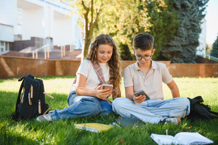 Students sitting on green grass, interacting with smartphones outdoors. Modern technology impacting...