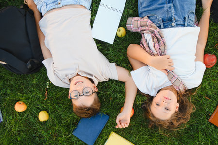 Children lying on fresh green grass with school books and apples, enjoying a break from learning outdoorsの写真素材