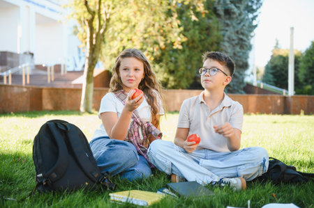 School children sitting on campus grass, having a healthy snack with apples during a school break...