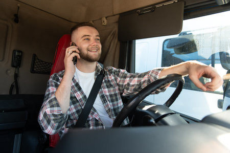 Young man driving a truck, smiling and communicating on a mobile phone, representing modern...
