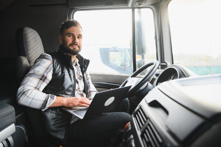 Professional truck driver sitting in cabin, using a laptop, managing logistics, and connecting through technology and remote workingの写真素材