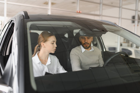 Saleswoman sitting inside a car with a male customer, discussing features and options in an...