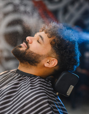 Man in barber chair receiving a soothing hair spray treatment. Experiencing wellness and grooming services in a salonの写真素材