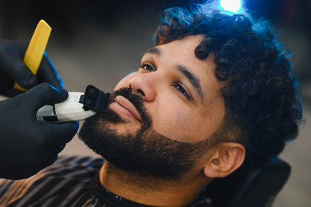 Man getting a beard trim from a barber in black gloves, focusing on precise grooming and styling in a modern salonの写真素材