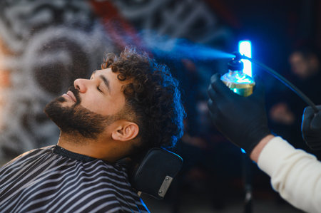 Man with curly hair and beard enjoying a barber spraying his hair for styling and grooming in a modern salonの写真素材