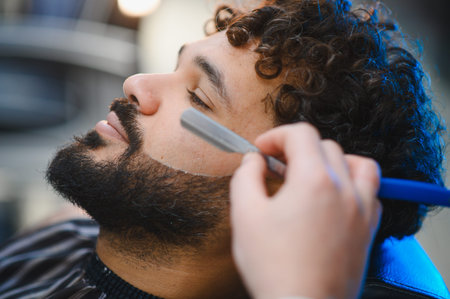 Barbershop close up of barber shaving a bearded man's face with a straight razor, precise grooming...