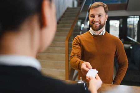 Guest smiling while receiving room key card from receptionist at the hotel check in desk, enjoying hospitality serviceの写真素材