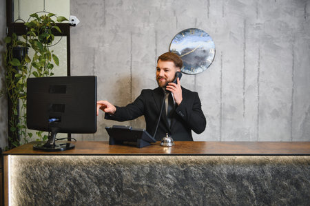 Professional hotel receptionist providing excellent customer service on phone, using computer at a modern reception deskの写真素材