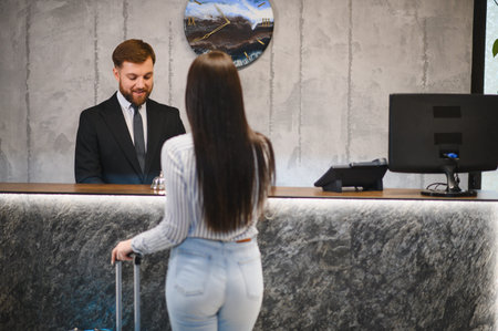 Hotel receptionist assisting a female guest arriving with luggage at the front desk, providing hospitality serviceの写真素材