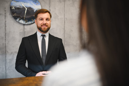 Smiling bearded businessman in a suit talking with an unrecognizable colleague in a modern office meeting room. Concept of corporate communication and discussionの写真素材