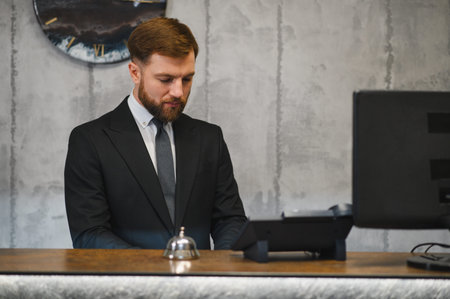 Professional bearded man in suit working at hotel reception, providing hospitality service to guests in a modern lobbyの写真素材