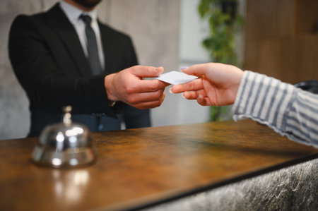 Hotel staff exchanging room key card with a guest at the reception desk, focusing on hospitality and serviceの写真素材