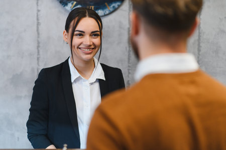 Friendly receptionist welcoming and assisting a male guest at the hotel reception desk, providing quality customer serviceの写真素材