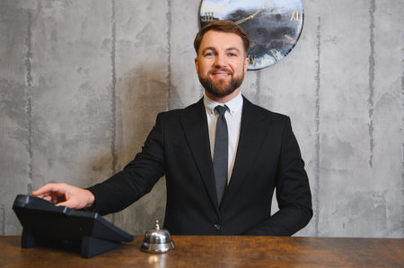 Smiling man working at front desk, providing professional hospitality service. He is representing customer satisfaction and supportの写真素材