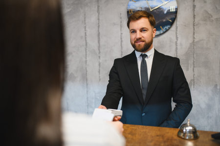 Professional hotel desk clerk presenting terminal for contactless card payment, providing friendly and efficient customer serviceの写真素材