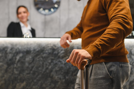Traveler standing with luggage at a modern hotel reception desk, a blurred receptionist assists with check in processの写真素材