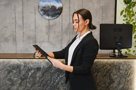 Young woman working as a hotel or business center receptionist, managing guest inquiries and performing professional dutiesの写真素材