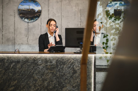 Customer service agent working at hotel reception desk, talking on telephone and using tablet for reservationsの写真素材