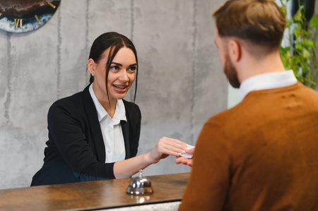 Hotel receptionist smiling, passing an electronic key card to a guest during check in at the reception desk. Providing hospitalityの写真素材