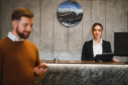Female hotel receptionist smiling, welcoming a male guest checking into the modern hotel lobby. Hospitality service conceptの写真素材
