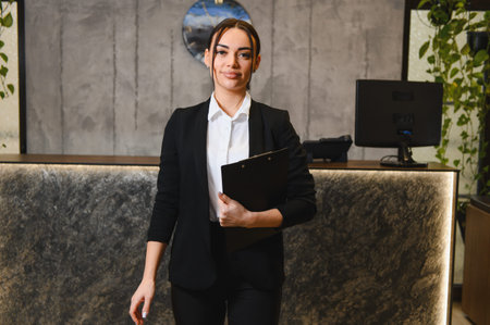 Young woman working in hospitality, welcoming guests at a modern reception desk, demonstrating professional service and efficiencyの写真素材