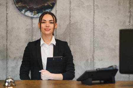 Young woman working as hotel concierge, providing professional hospitality service while standing at receptionの写真素材