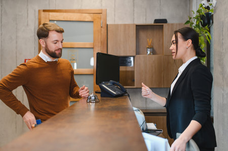 Smiling man interacting with female receptionist, completing check in process at modern hotel lobby. Offering hospitality serviceの写真素材