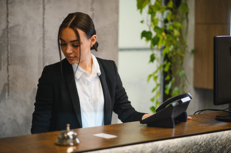 Young professional receptionist managing front desk operations in a modern hotel lobby, providing concierge and customer serviceの写真素材