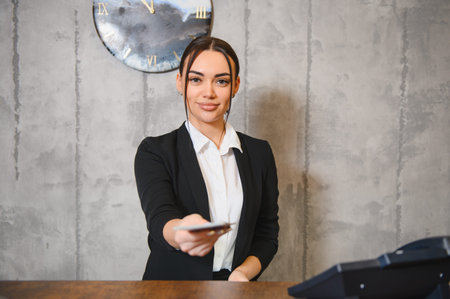 Friendly hotel receptionist extending a key card to a guest, providing professional customer service at a modern front deskの写真素材