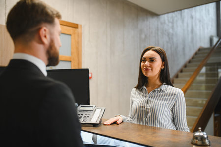 Woman smiling, interacting with a male receptionist for a seamless check in process at a modern hotelの写真素材