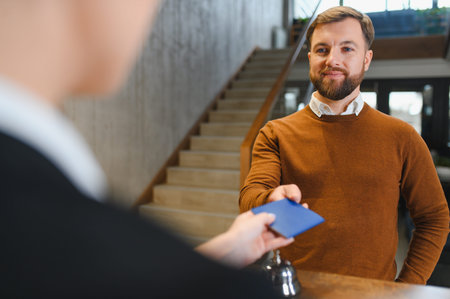 Man smiling at hotel receptionist, handing over passport or document during check in process. Travel and hospitalityの写真素材