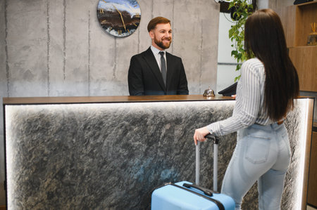 Smiling receptionist assisting a female guest with suitcase at modern hotel counter, providing professional hospitality serviceの写真素材