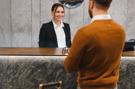 Smiling hotel receptionist providing service and greeting a customer at the front desk. Hospitality and travel industry conceptの写真素材
